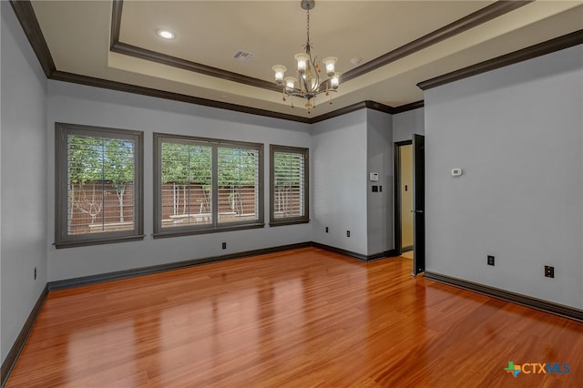 empty room with light hardwood / wood-style floors, a raised ceiling, an inviting chandelier, and ornamental molding