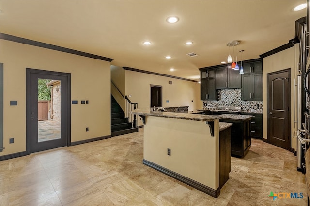 kitchen featuring dark stone counters, an island with sink, crown molding, a breakfast bar, and pendant lighting