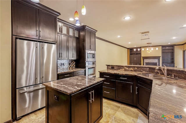 kitchen with dark brown cabinetry, sink, appliances with stainless steel finishes, dark stone countertops, and hanging light fixtures