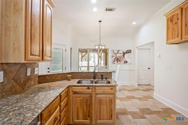 kitchen with backsplash, crown molding, sink, hanging light fixtures, and light stone counters