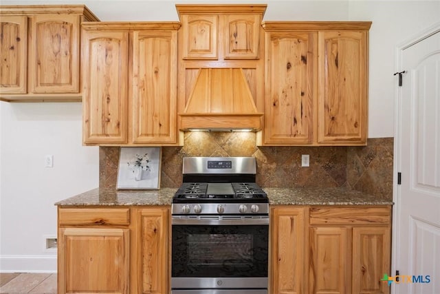 kitchen with premium range hood, dark stone counters, gas range, decorative backsplash, and light tile patterned flooring