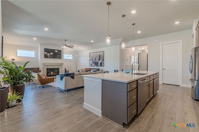 kitchen with sink, light hardwood / wood-style flooring, a kitchen island with sink, stainless steel appliances, and light stone countertops