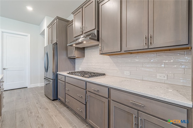 kitchen with stainless steel appliances, light stone countertops, light hardwood / wood-style floors, and backsplash