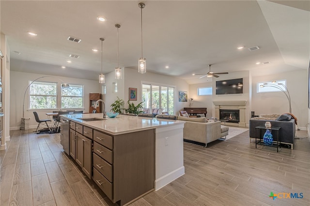 kitchen with sink, a center island with sink, pendant lighting, ceiling fan, and light stone countertops