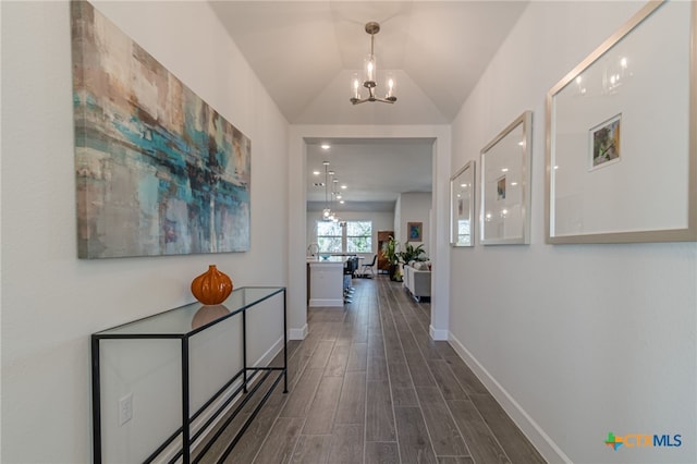 corridor with lofted ceiling, dark hardwood / wood-style floors, and a notable chandelier