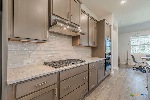 kitchen with tasteful backsplash, stainless steel appliances, light stone counters, and light wood-type flooring