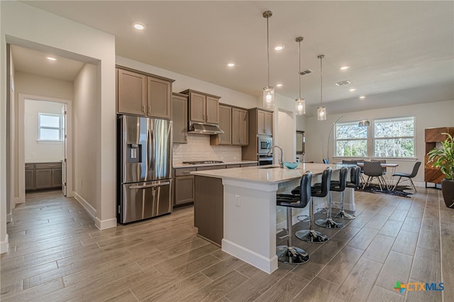 kitchen featuring an island with sink, a kitchen bar, hanging light fixtures, light hardwood / wood-style floors, and stainless steel appliances