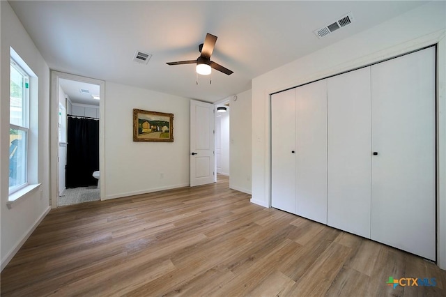 unfurnished bedroom with ceiling fan, ensuite bath, multiple windows, and light wood-type flooring