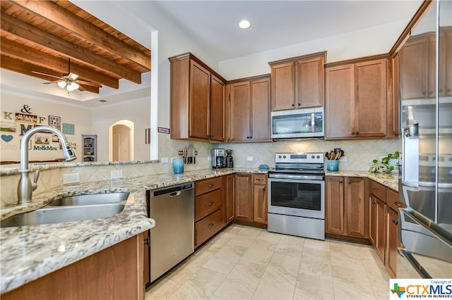 kitchen featuring stainless steel appliances, beamed ceiling, sink, light stone countertops, and decorative backsplash