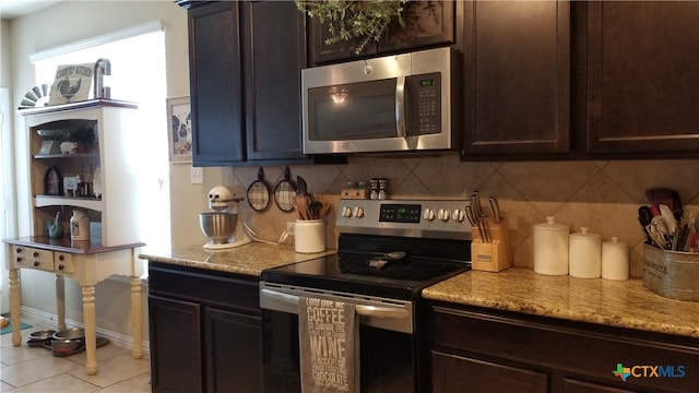 kitchen with dark brown cabinetry, light stone counters, appliances with stainless steel finishes, light tile patterned floors, and backsplash