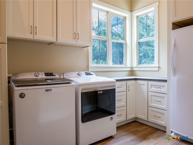 clothes washing area featuring cabinets, washer and dryer, and light hardwood / wood-style flooring