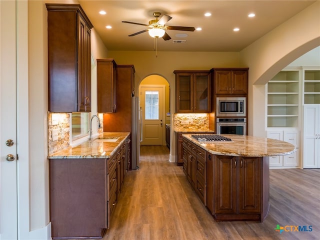 kitchen with stainless steel appliances, wood-type flooring, a center island, sink, and tasteful backsplash