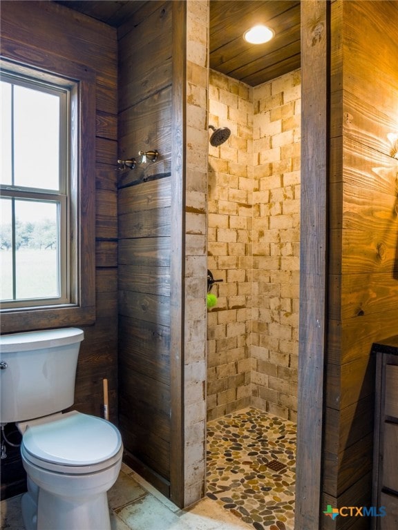 bathroom featuring toilet, wooden walls, and tiled shower