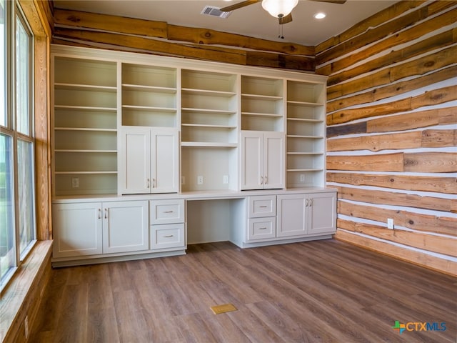 unfurnished office featuring hardwood / wood-style floors, built in desk, ceiling fan, and log walls