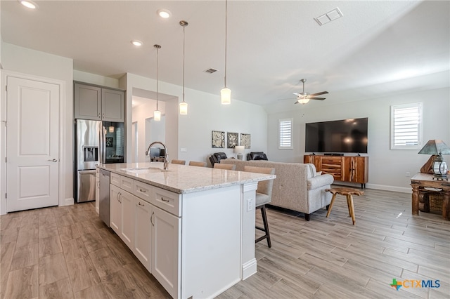 kitchen with a breakfast bar, sink, hanging light fixtures, a kitchen island with sink, and light stone counters