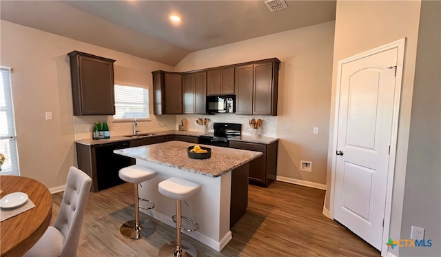 kitchen with light stone countertops, a center island, sink, hardwood / wood-style floors, and black appliances