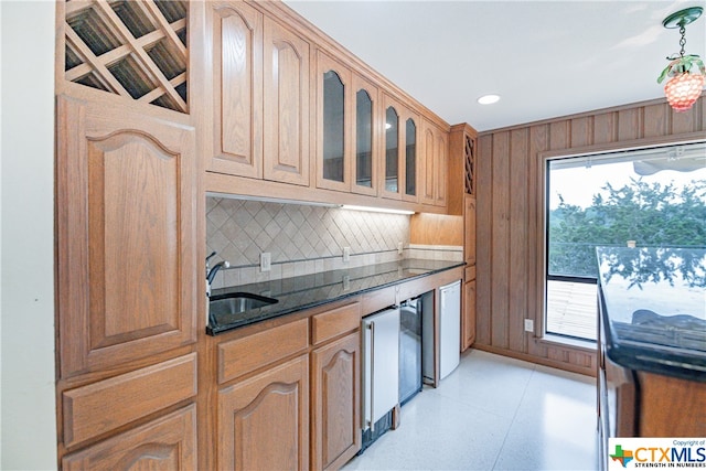 kitchen featuring pendant lighting, dark stone countertops, sink, and wooden walls