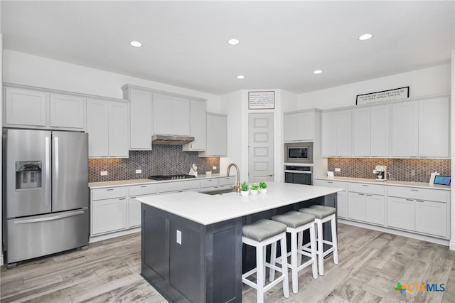 1386 Lyme Park, Bulverde, TX 78163 - kitchen featuring stainless steel appliances, under cabinet range hood, a breakfast bar area, light wood finished floors, and tasteful backsplash