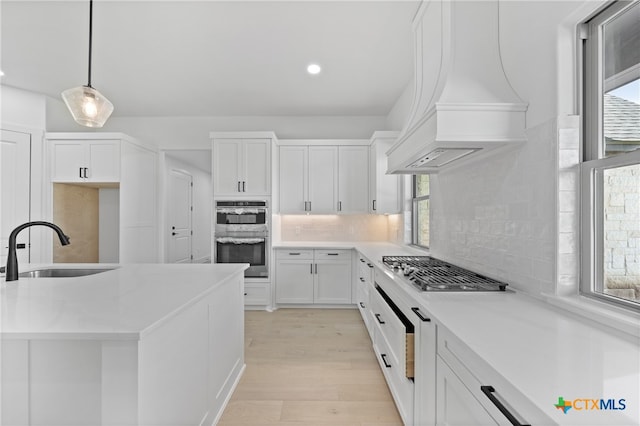 kitchen featuring custom exhaust hood, white cabinets, sink, and plenty of natural light