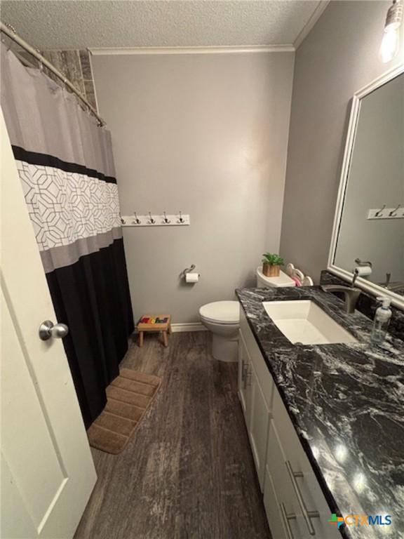 bathroom featuring toilet, wood-type flooring, a textured ceiling, ornamental molding, and vanity