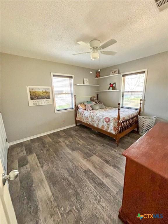 bedroom with ceiling fan, dark hardwood / wood-style floors, multiple windows, and a textured ceiling