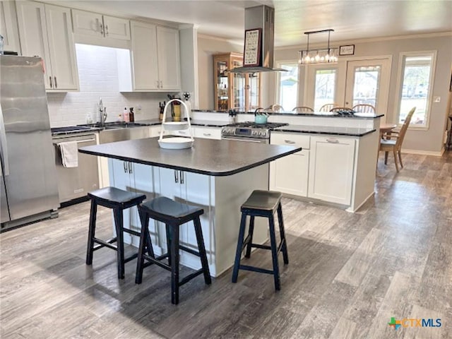 kitchen with pendant lighting, a breakfast bar area, island exhaust hood, kitchen peninsula, and stainless steel appliances