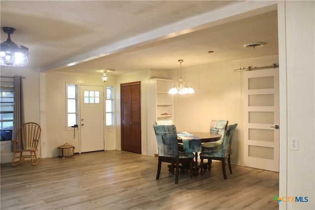 dining space with built in features, wood-type flooring, and an inviting chandelier