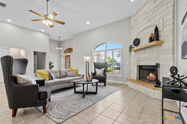 living room with ceiling fan, a stone fireplace, light tile patterned floors, and high vaulted ceiling