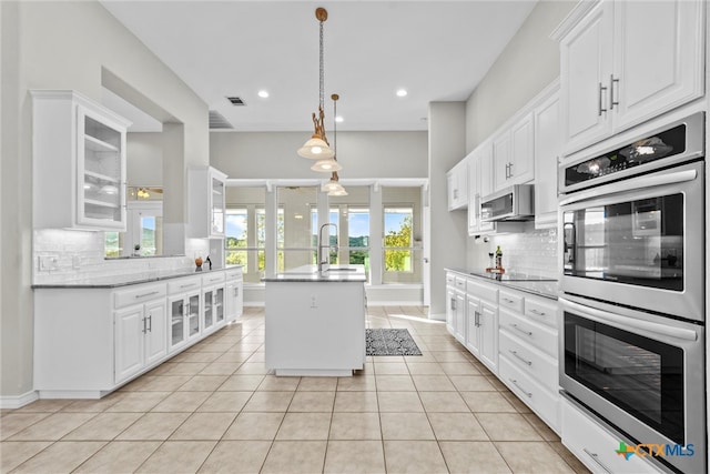 kitchen featuring decorative backsplash, a kitchen island, light stone countertops, white cabinetry, and appliances with stainless steel finishes