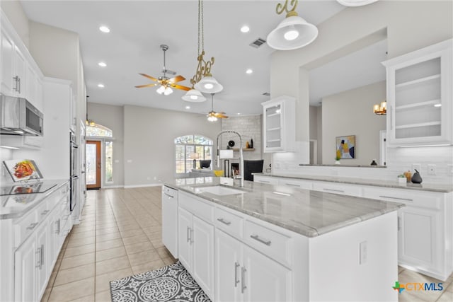 kitchen with light tile patterned flooring, a center island with sink, white cabinetry, hanging light fixtures, and ceiling fan