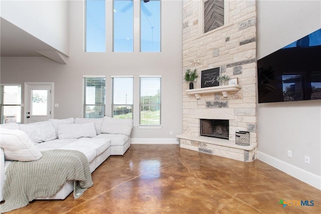 living room with a stone fireplace, a towering ceiling, and concrete floors