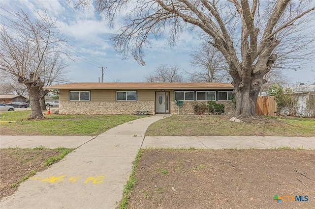 ranch-style house featuring stone siding, a front lawn, and fence