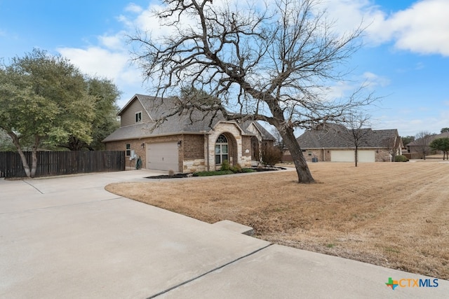 view of front of property with brick siding, concrete driveway, roof with shingles, fence, and a front yard