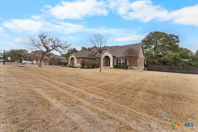 french country inspired facade with a front yard, stone siding, and fence