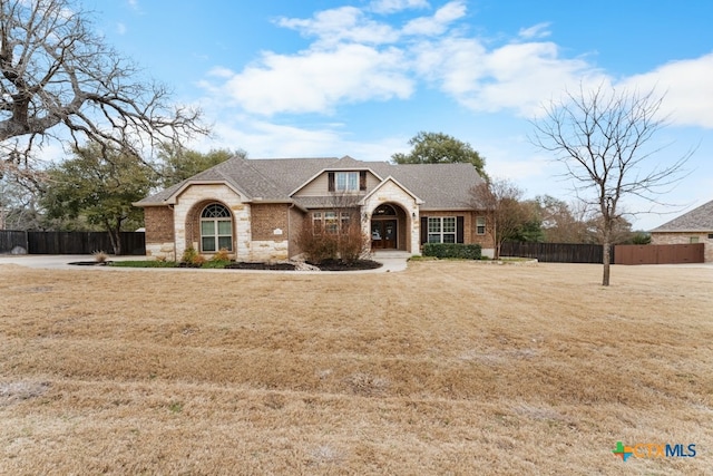 view of front of house featuring a shingled roof, stone siding, fence, a front yard, and brick siding