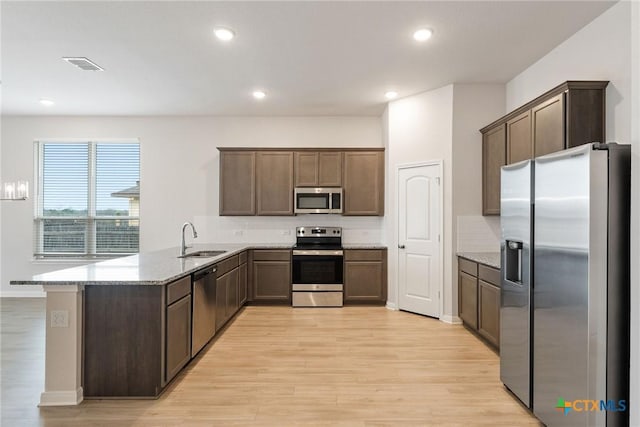 kitchen featuring sink, kitchen peninsula, stainless steel appliances, light stone countertops, and light hardwood / wood-style flooring