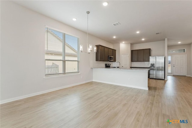 kitchen with appliances with stainless steel finishes, hanging light fixtures, dark brown cabinetry, kitchen peninsula, and light wood-type flooring