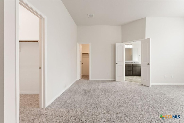 unfurnished bedroom with light carpet, connected bathroom, a spacious closet, and a closet