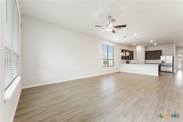 unfurnished living room featuring hardwood / wood-style flooring, sink, and ceiling fan with notable chandelier