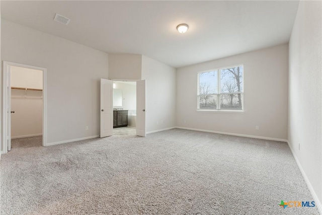 unfurnished bedroom with ensuite bathroom, a spacious closet, and light colored carpet