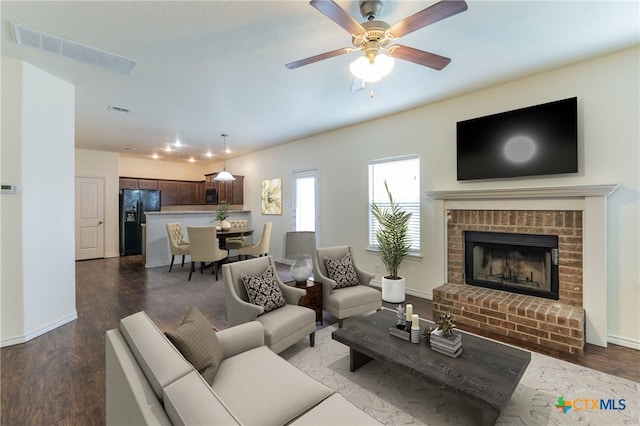 living room with dark wood-type flooring, ceiling fan, and a brick fireplace