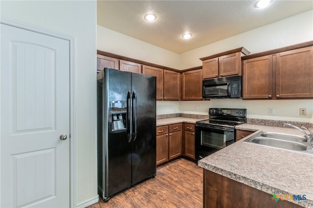 kitchen with black appliances, hardwood / wood-style floors, sink, and a textured ceiling