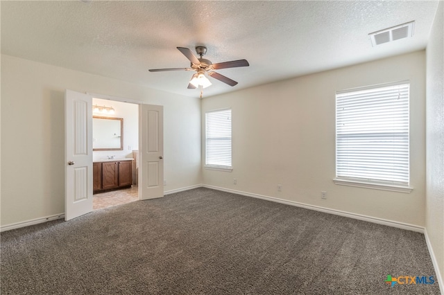 unfurnished bedroom featuring ceiling fan, multiple windows, a textured ceiling, and dark carpet