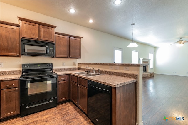 kitchen featuring wood-type flooring, kitchen peninsula, hanging light fixtures, black appliances, and sink