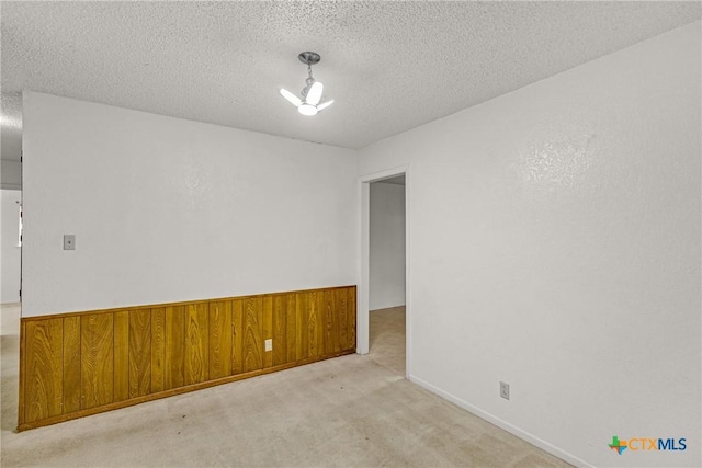 spare room with light carpet, a textured ceiling, and wood walls