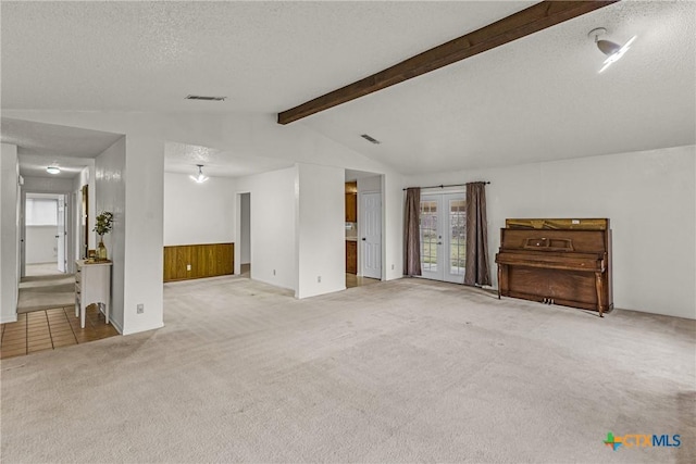 unfurnished living room featuring wooden walls, french doors, light colored carpet, and a textured ceiling