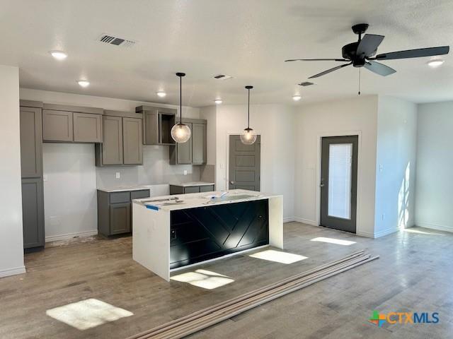 kitchen with visible vents, hanging light fixtures, gray cabinets, and a kitchen island with sink