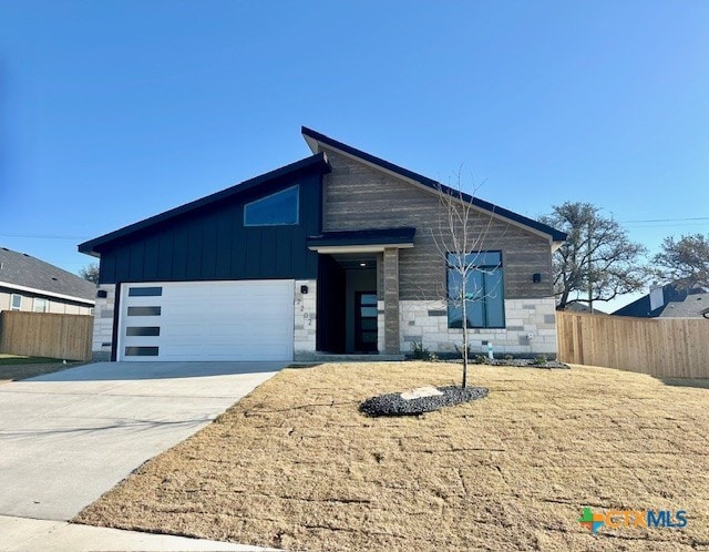 contemporary house featuring stone siding, concrete driveway, fence, and an attached garage