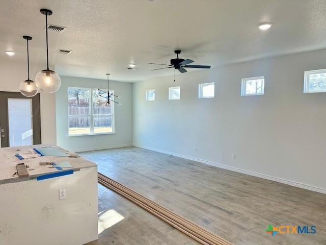 kitchen with a textured ceiling, visible vents, baseboards, open floor plan, and decorative light fixtures