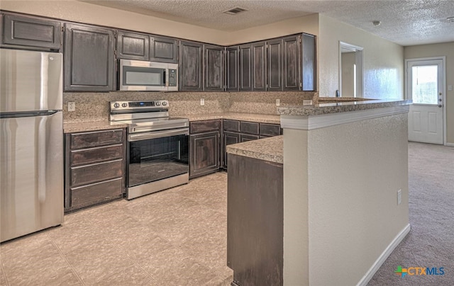 kitchen featuring kitchen peninsula, appliances with stainless steel finishes, a textured ceiling, and dark brown cabinetry